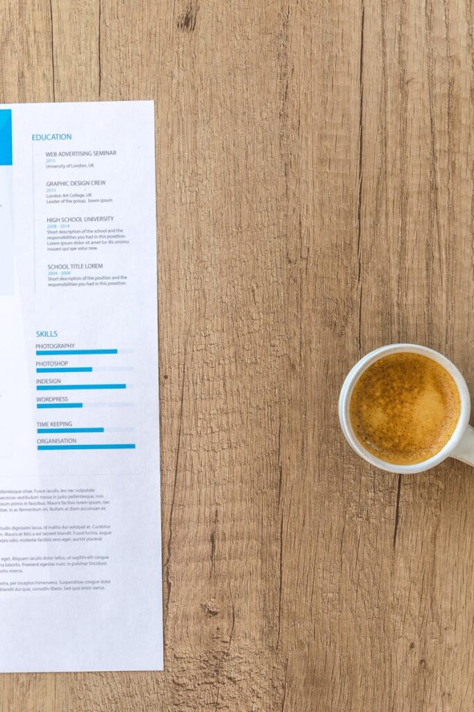 Top view of a desk with resume, coffee cup, and laptop on a wooden surface, ideal for business concepts.